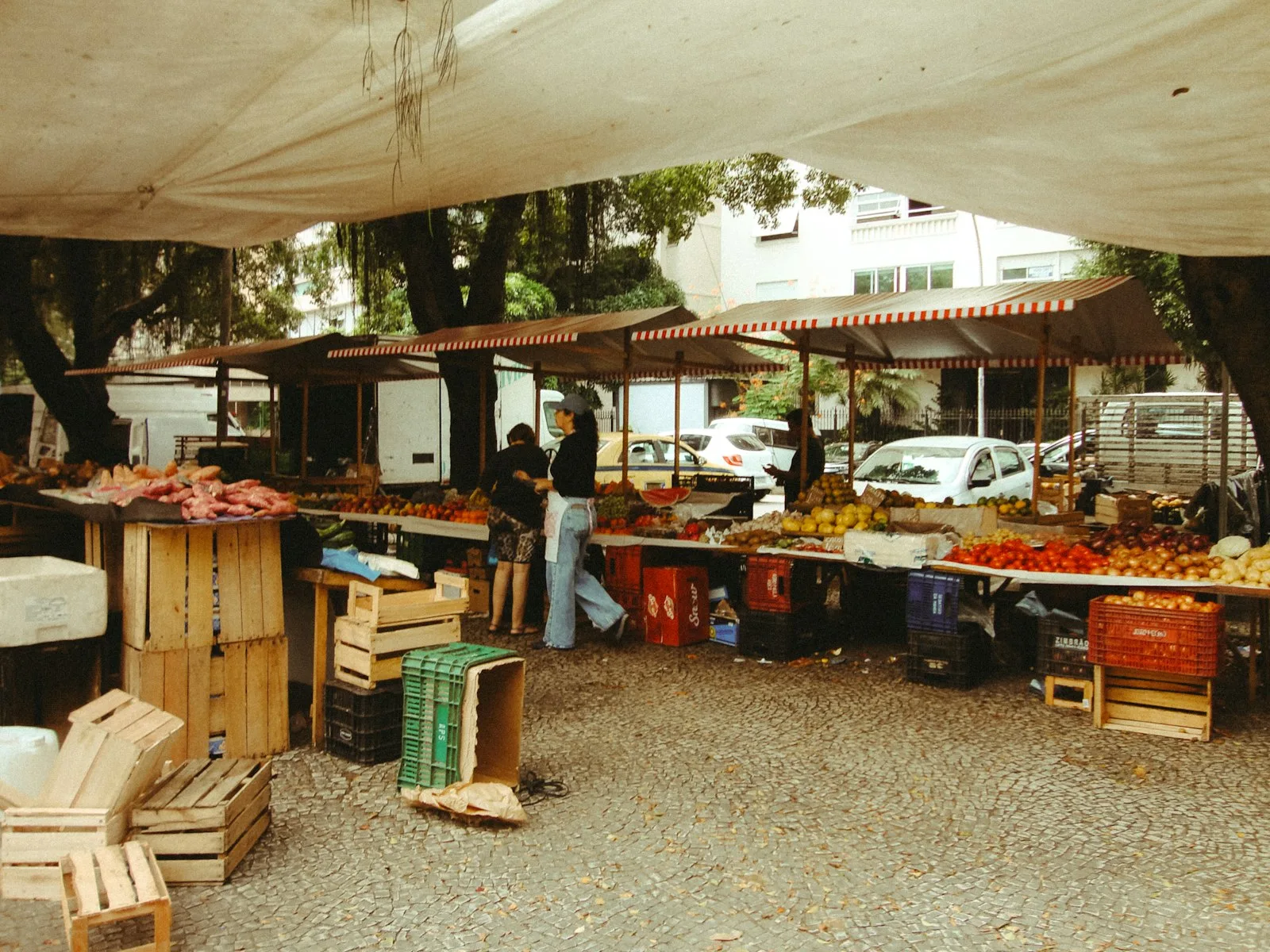 Outdoor market stalls under striped awnings, with tomatoes, onions and fruit stacked beside timber crates
